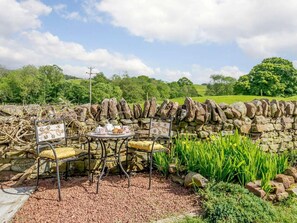 Eine Steinsäule mit Tisch und Stühlen für das Essen im Freien, umgeben von viel Grün und blauem Himmel.