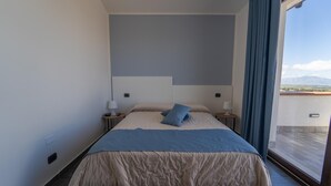 Een slaapkamer met een bed, twee nachtkastjes, een raam met gordijnen en uitzicht op het omliggende landschap.
