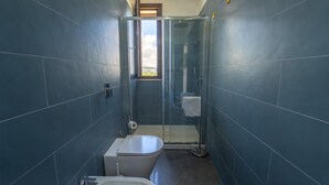 Een badkamer met toilet, douche en raam.