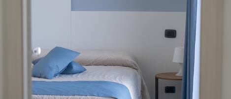 A bedroom with two beds, a bedside table, a lamp, and a wall-mounted switch.