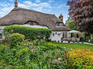 Ein traditionelles Haus mit Strohdach und einem Garten davor.