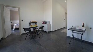 Una habitación de hotel moderna con cama, una mesa de comedor con sillas, una pequeña kitchenette y un escritorio con silla.
