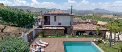 A two-story house with a swimming pool, a stone exterior, and a view of the countryside.
