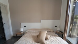 Una habitación de hotel con una cama grande, dos mesitas de noche con lámparas, una puerta y una ventana.