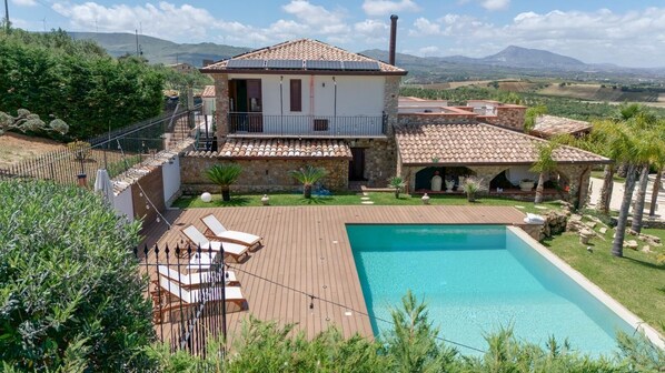 A villa with a swimming pool, a stone exterior, and a view of the countryside.