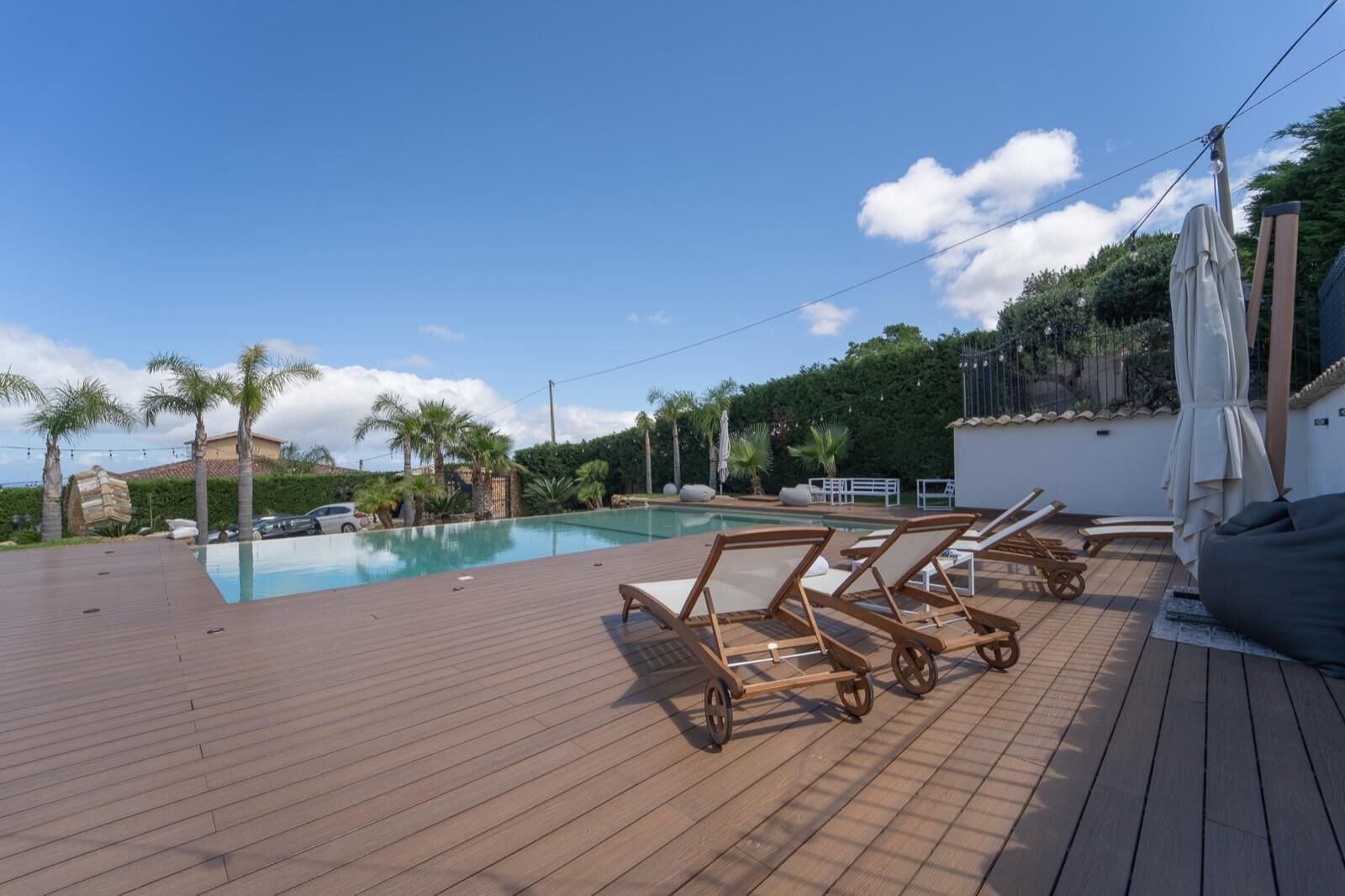 A wooden deck with a pool, lounge chairs, and palm trees.