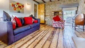 A room with a stone wall, a wooden ceiling, a leather sofa, a patterned armchair, and a wooden cabinet. - 2 Bed in Matlock (oc-83435) (Slaley)
