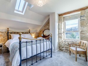 Ein Schlafzimmer mit einer Steinsäule, einem Bett mit Metallgestell, einem Holzstuhl und einem Fenster mit Blick.