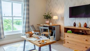 Una habitación con una mesa de comedor, sillas, un televisor, una planta y un ventanal con cortinas.