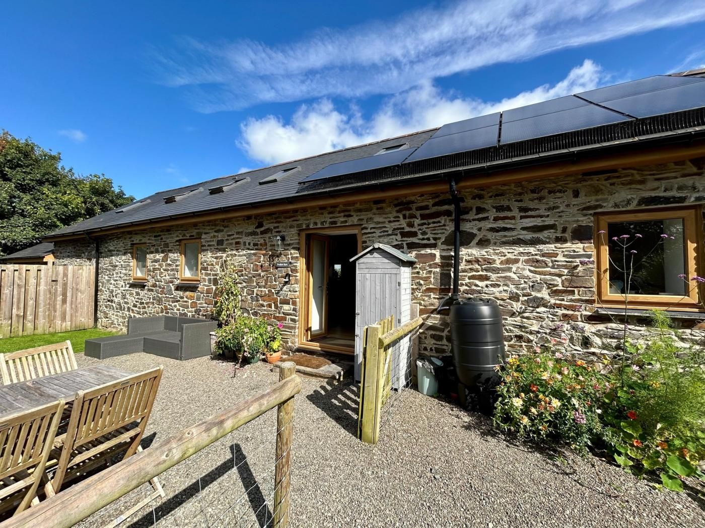 A stone building with a sloped roof, a wooden fence, and a gravel patio.