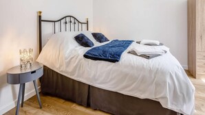 Een opgemaakt bed met kussens en dekbed, een nachtkastje met glazen, en een houten garderobe.