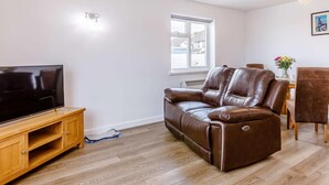 Een woonkamer met een leren bank, een tv-meubel van hout en een eettafel met stoelen.