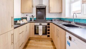 Een kleine keuken met houten kastjes, een inbouwoven, een spoelbak en een raam voor natuurlijk licht.
