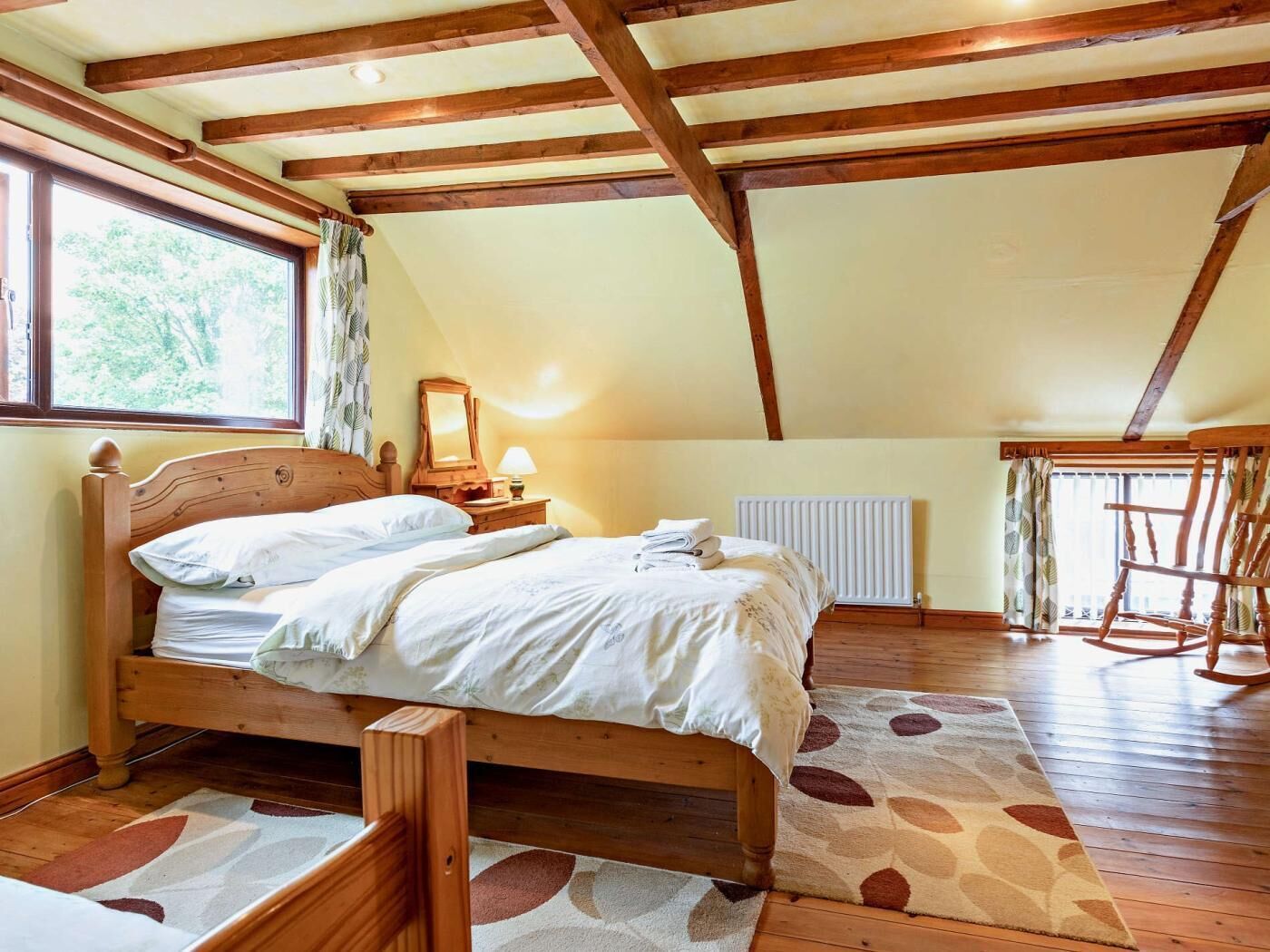 Een slaapkamer met een houten bed, een radiator, een schommelstoel en een raam met gordijnen.
