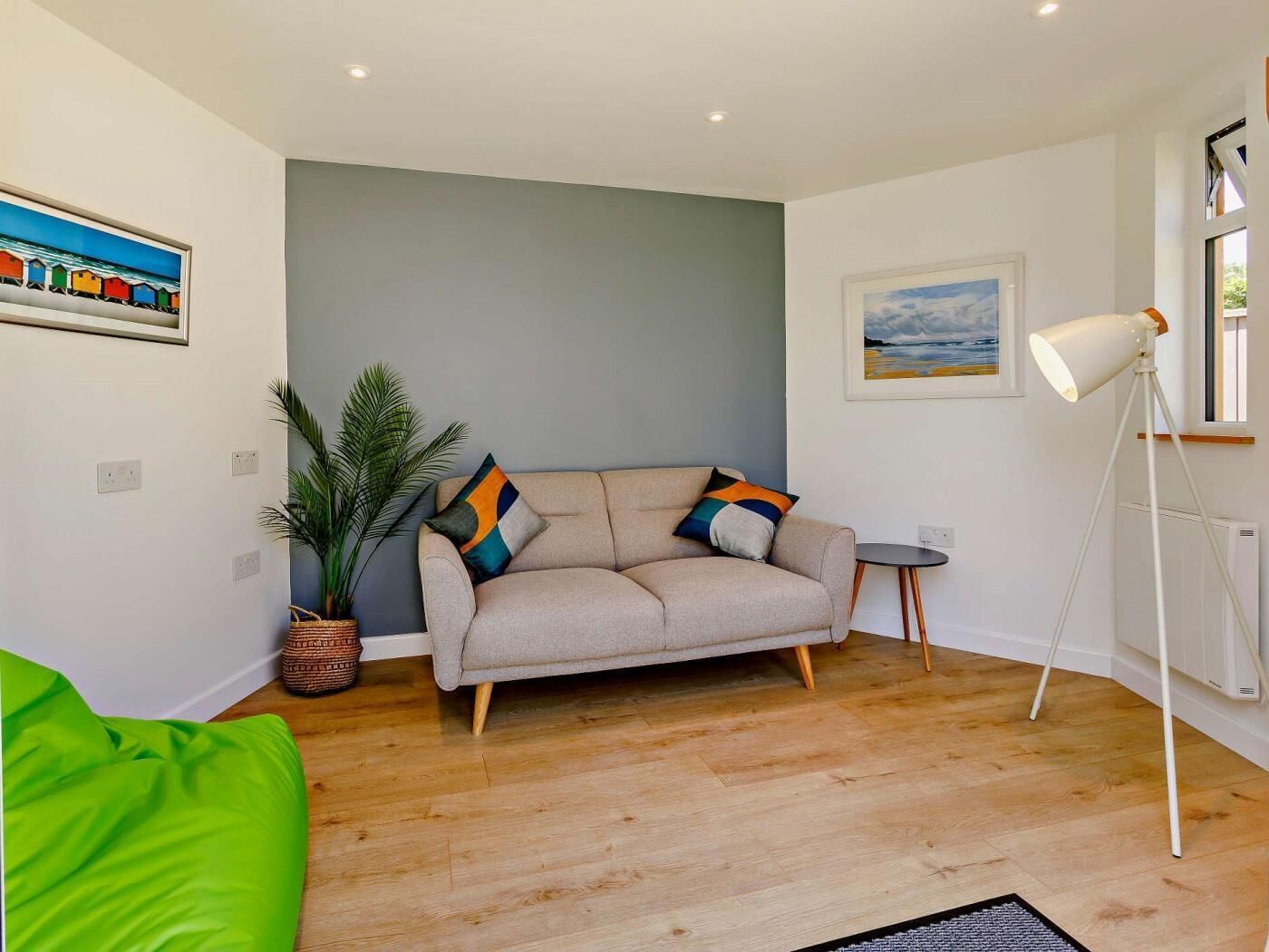 Een woonkamer met een bank, een tafeltje, een vloerlamp, een potplant en kunstwerken aan de muur.