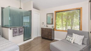 Un bagno moderno con cabina doccia in vetro, un lavabo con specchio e un'ampia finestra vista alberi.
