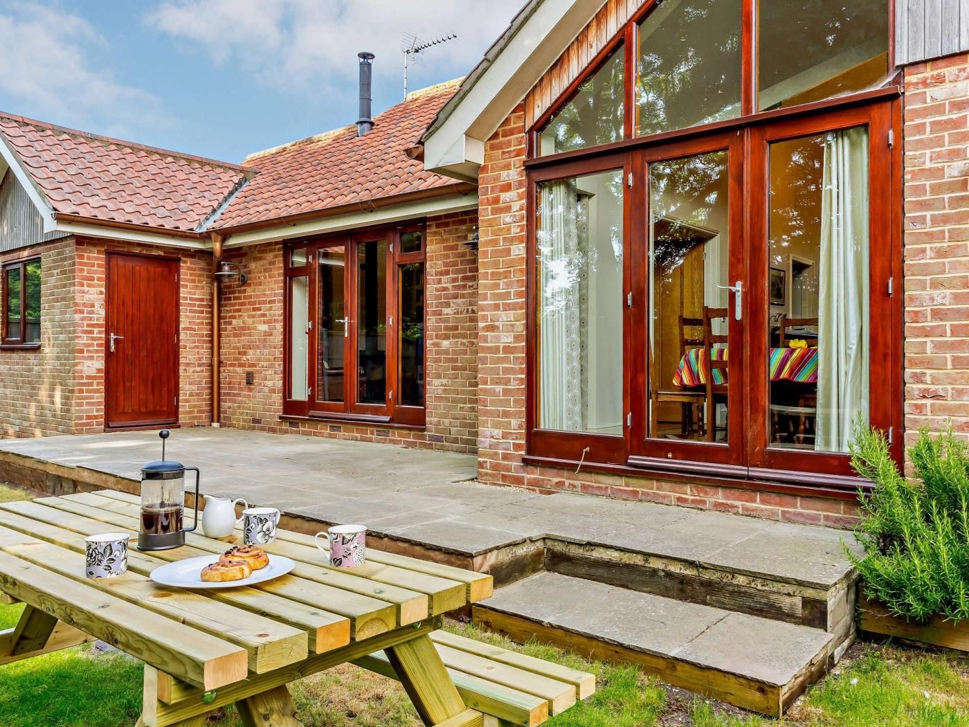 A brick house with a patio, a dining table with a plate of food and drinks, and a window with curtains.