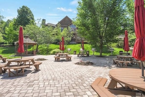 A patio area with picnic tables and red umbrellas, surrounded by greenery and a building in the background. - Large condo near Mountain Creek & Crystal Springs (Vernon Township)