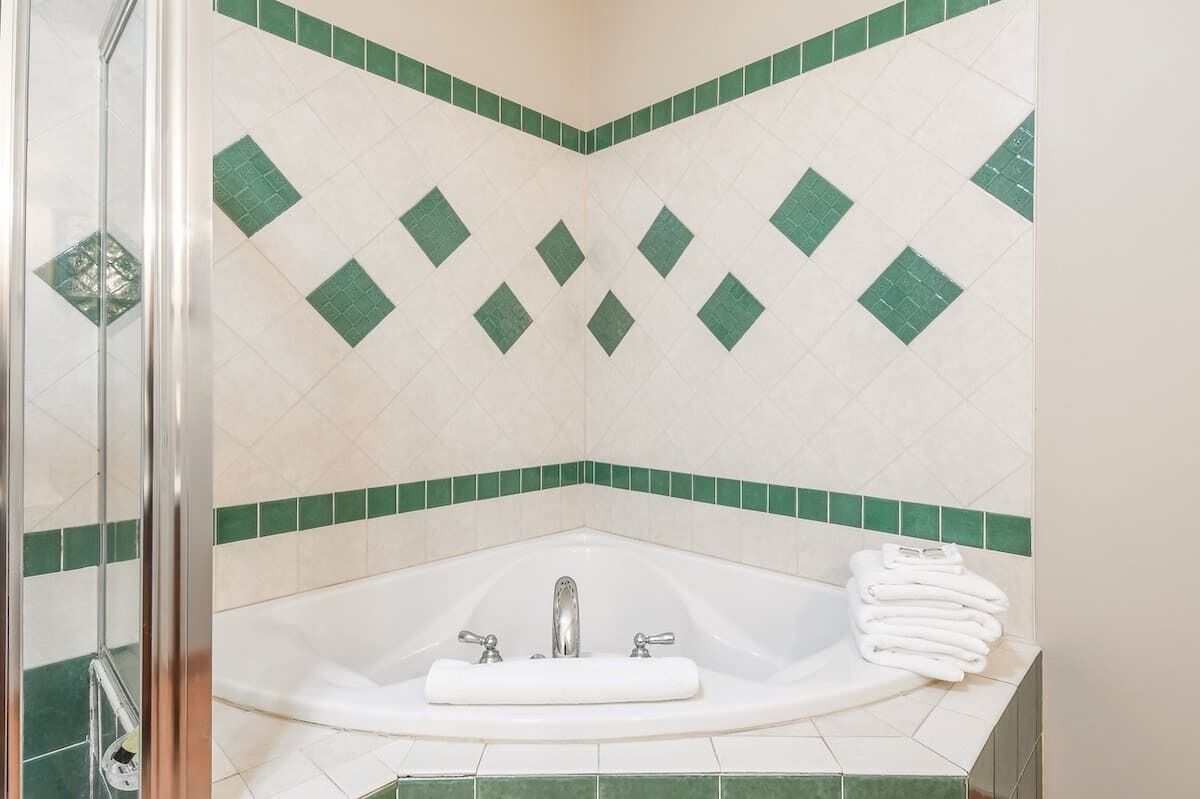 A bathroom with a shower, a bathtub with a white towel, and green and white patterned tiles.