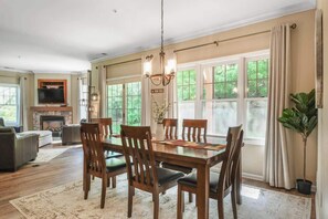 A dining area with a wooden table, chairs, a chandelier, and large windows with curtains. - Large condo near Mountain Creek & Crystal Springs (Vernon Township)