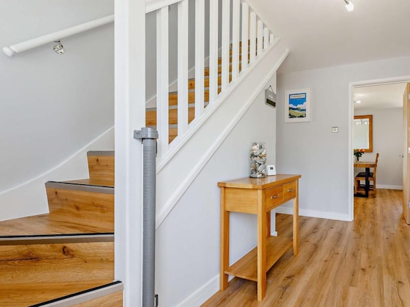 A staircase with wooden steps and white railings, a wooden console table with a vase, and a framed picture on the wall.