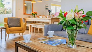 A modern living room with a wooden coffee table, a vase with flowers, a sofa, and a dining area in the background. - 5 Bed in Bridport (oc-83584) (Charmouth)