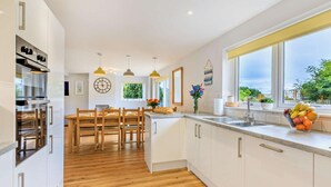 A modern kitchen with white cabinets, a wooden dining table, and a fruit bowl on the counter. - 5 Bed in Bridport (oc-83584) (Charmouth)