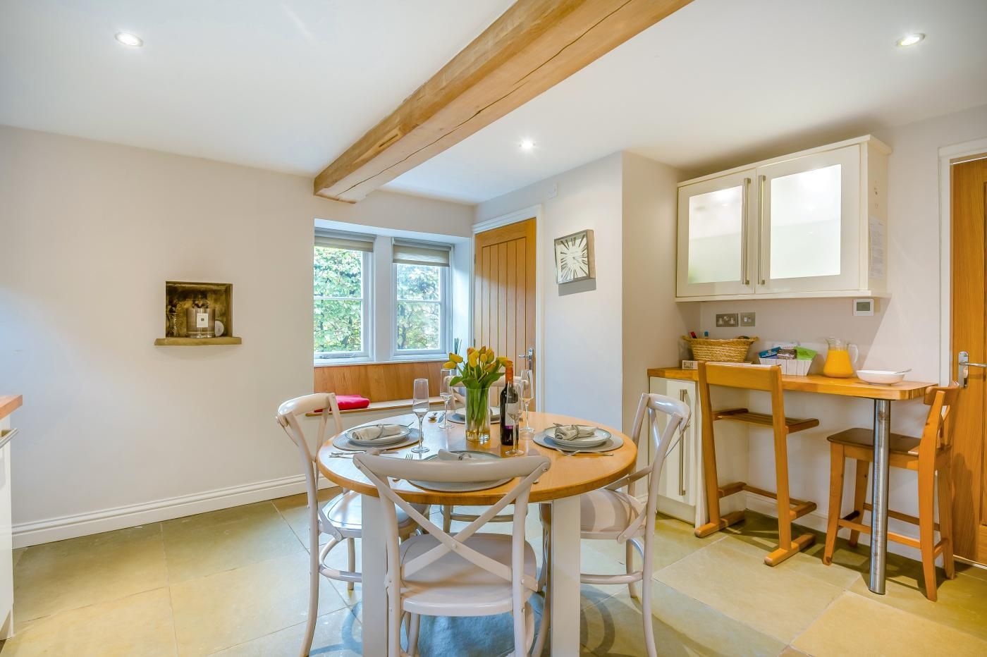 A dining area with a round table, white chairs, and a wooden ceiling beam.