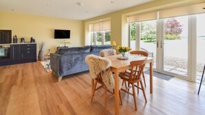 A modern living room with a sofa, a dining table with chairs, a kitchen area, and a large sliding glass door leading to a garden. - 1 Bed in Corsham (oc-83690) (Box)