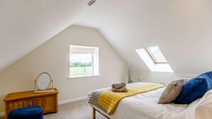A bedroom with a sloped ceiling, a skylight, a bed with a yellow blanket, a wooden nightstand, and a blue ottoman. - 1 Bed in Corsham (oc-83690) (Box)