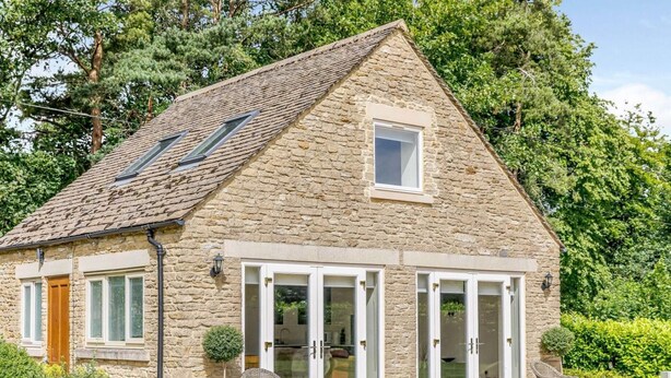 A stone house with a sloped roof, large glass doors, and a gravel driveway. - 1 Bed in Corsham (oc-83690) (Box)