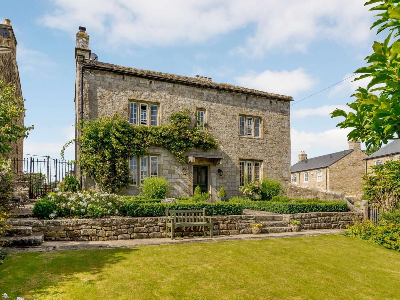A stone building with a garden, a bench, and a clock tower.