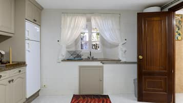 A kitchen with white cabinets, a window with sheer curtains, a wooden door, and a kitchen mat.