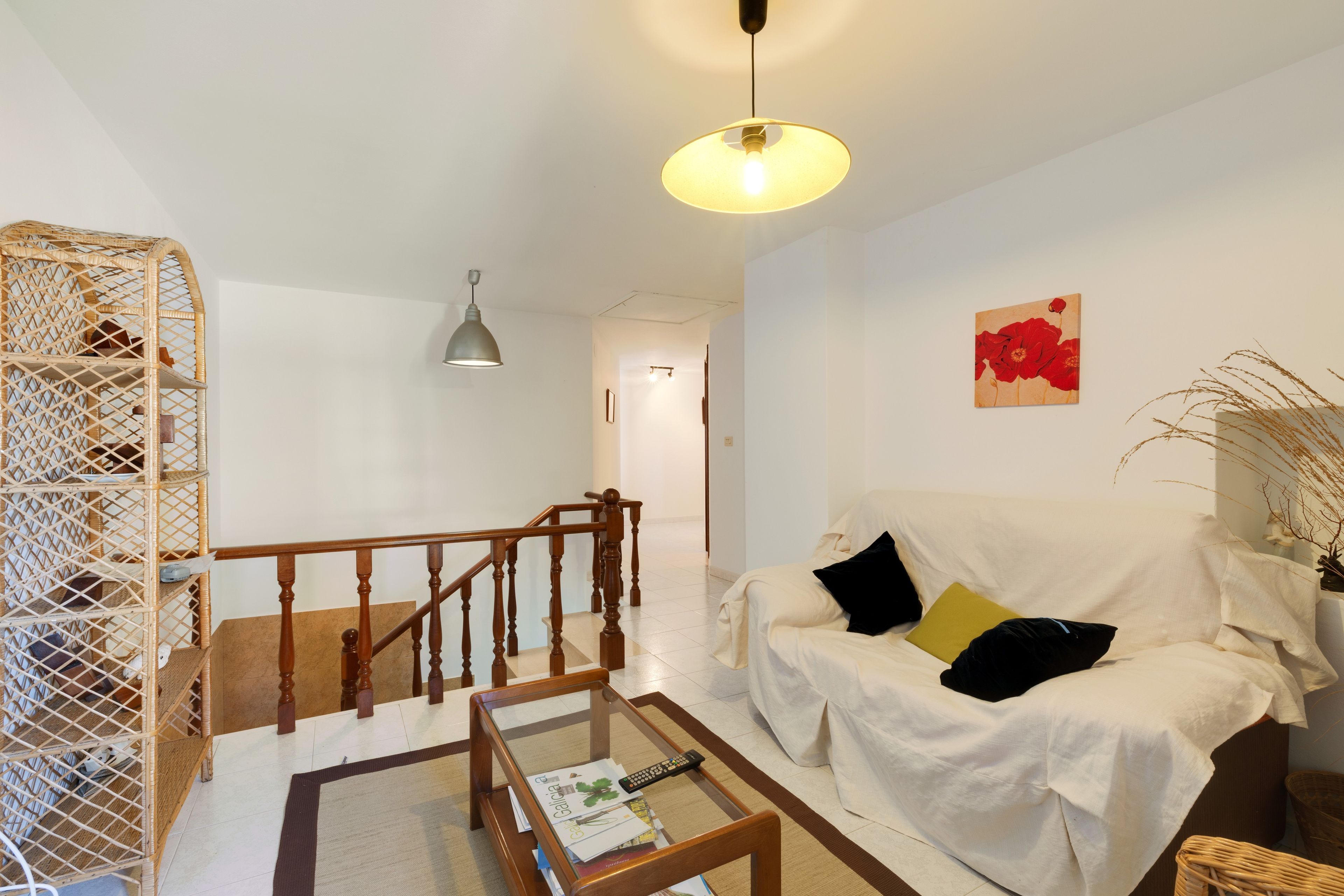 Una sala de estar con escalera de madera, un sofá blanco, una mesa de centro de vidrio y una lámpara colgante.
