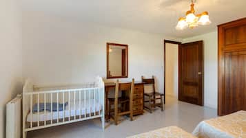 Een kamer met een ledikantje, een houten bureau met lades, een stoel, een spiegel en een kledingkast.