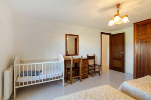 A room with a crib, a wooden desk with drawers, a chair, a mirror, and a wardrobe.