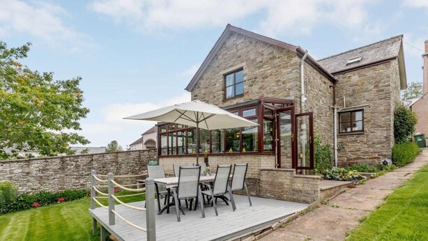 A stone house with a patio, outdoor seating, and a view of the garden.