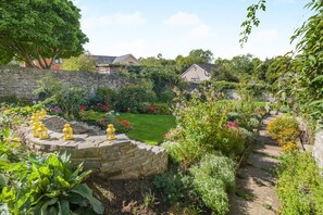 A garden with a stone wall, a grassy lawn, and various plants and flowers.