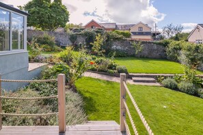 A well-maintained garden with a wooden deck, stone walls, and a variety of plants and flowers.
