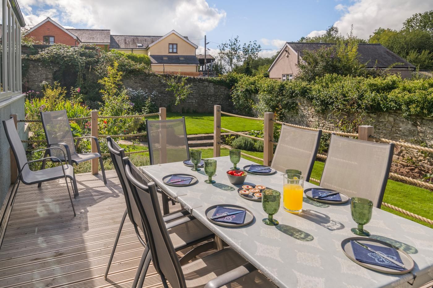 An outdoor dining area with a table set for four, surrounded by chairs, and a stone wall in the background.