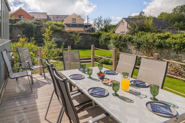 An outdoor dining area with a table set for four, surrounded by chairs, and a stone wall in the background.