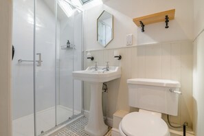 Une salle de bain avec une douche à parois de verre, un lavabo sur colonne, des toilettes et un miroir au-dessus du lavabo.