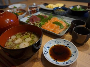 A dining table with various dishes, including a bowl of soup, a plate of sashimi, and a small bowl of soy sauce.