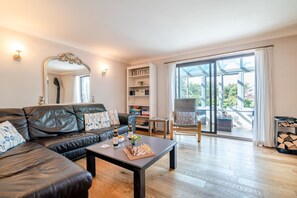 A modern living room with a leather sofa, a coffee table with chess pieces, a bookshelf, and a view through large glass doors to an outdoor area.