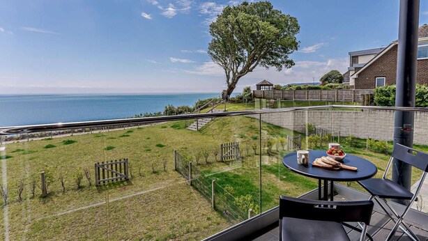 Ein Balkon mit Tisch und Stühlen, der auf eine Grünfläche und den Blick aufs Meer bietet.