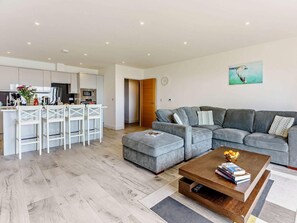Ein modernes Wohnzimmer mit grauem Sofa, einem Couchtisch und einer Küchenzeile mit weißen Schränken sowie einem Esstisch.
