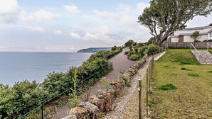 Ein Küstenweg mit Blick auf das Meer, einer Grünfläche und einem Gebäude mit einer Treppe.