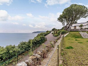 Ein Küstenweg mit Blick auf das Meer, einer Grünfläche und einem Gebäude mit einer Treppe.