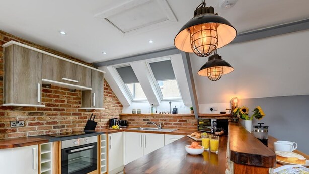 A modern kitchen with a brick wall, skylights, a wooden countertop, and a hanging light fixture. - 2 Bed in Morpeth (oc-83597) (Rothbury)
