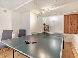 Una mesa de ping pong con dos paletas, una silla, un estante con objetos y un armario de madera.